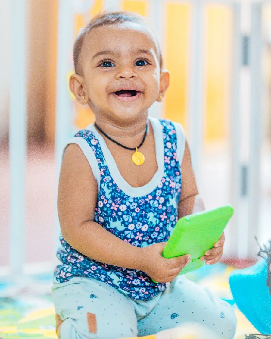 Smiling baby sitting on a play mat holding a green toy